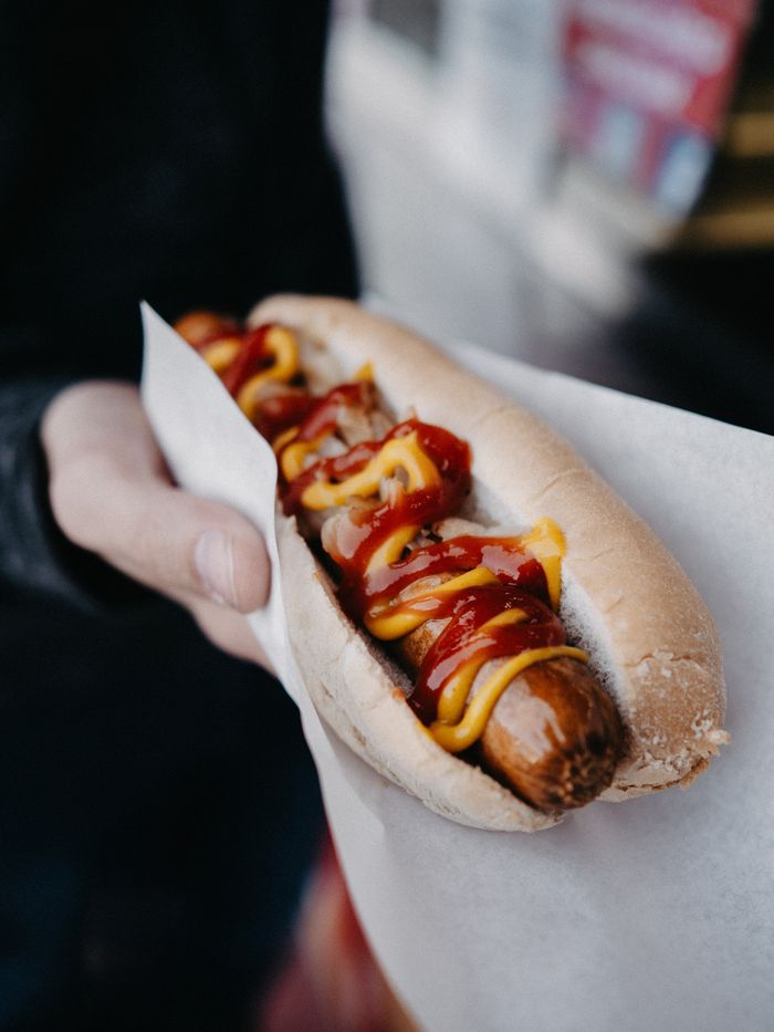 Appetizing hot dog with mustard and ketchup held in hand, ready for lunch.